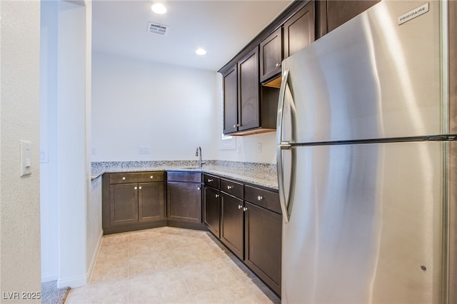 8665 Jerlyn St, Las Vegas, NV 89113 - kitchen featuring freestanding refrigerator, dark brown cabinetry, light stone countertops, recessed lighting, and light tile patterned flooring