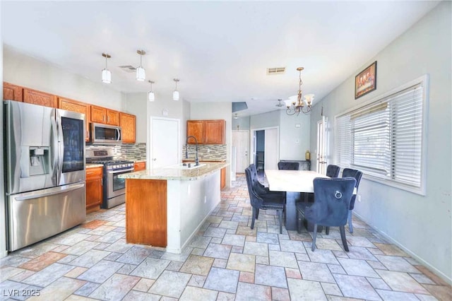 6233 Overhang Ave, Henderson, NV 89011 - kitchen with stainless steel appliances, a chandelier, brown cabinets, tasteful backsplash, and stone tile flooring