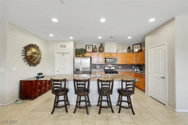 703 Shiva St, Las Vegas, NV 89178 - kitchen with appliances with stainless steel finishes, a sink, decorative backsplash, a center island with sink, and baseboards