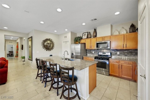 703 Shiva St, Las Vegas, NV 89178 - kitchen with stainless steel appliances, a sink, tasteful backsplash, an island with sink, and light stone countertops