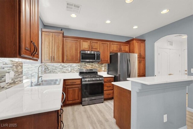 10845 Drake Ridge Ave, Las Vegas, NV 89166 - kitchen featuring appliances with stainless steel finishes, a sink, arched walkways, light wood-type flooring, and brown cabinetry