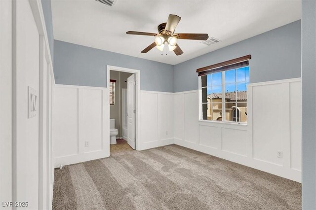 10845 Drake Ridge Ave, Las Vegas, NV 89166 - unfurnished bedroom featuring carpet, a decorative wall, a wainscoted wall, connected bathroom, and ceiling fan