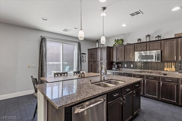 6857 Stone Tower Ct, Las Vegas, NV 89149 - kitchen with stainless steel appliances, a sink, tasteful backsplash, an island with sink, and dark stone countertops