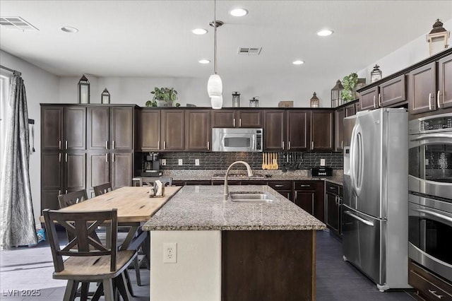 6857 Stone Tower Ct, Las Vegas, NV 89149 - kitchen featuring appliances with stainless steel finishes, a sink, dark brown cabinetry, light stone counters, and backsplash