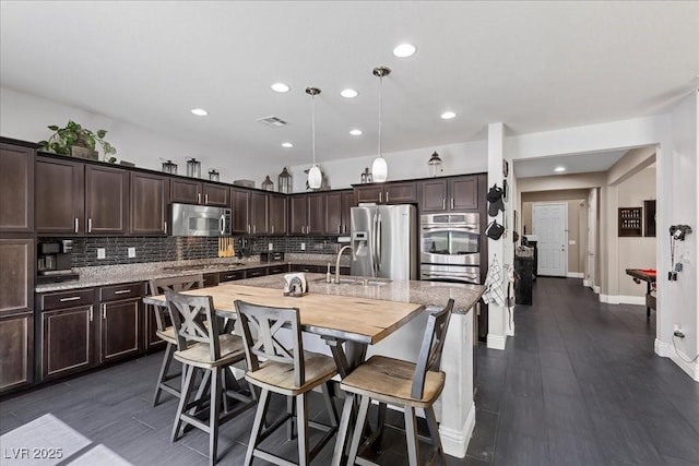 6857 Stone Tower Ct, Las Vegas, NV 89149 - kitchen featuring stainless steel appliances, dark brown cabinetry, tasteful backsplash, a center island with sink, and a sink