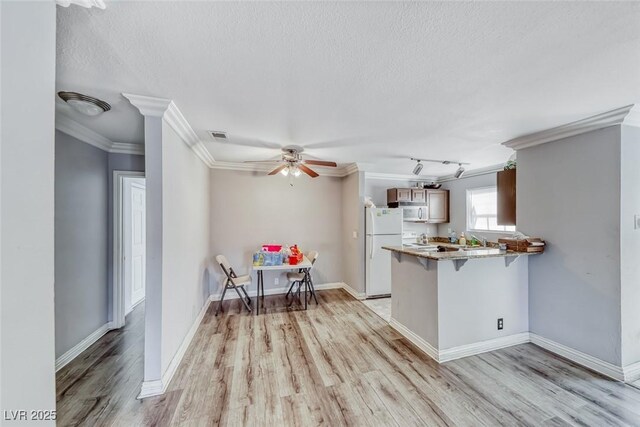 4050 Pacific Harbors Dr Unit 245, Las Vegas, NV 89121 - kitchen with freestanding refrigerator, a peninsula, light wood finished floors, a kitchen bar, and ornamental molding