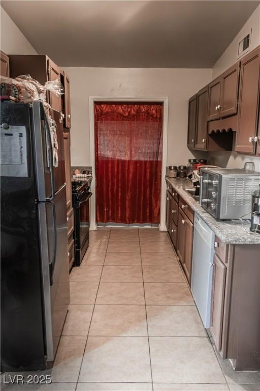 2001 E Mcwilliams Ave, Las Vegas, NV 89101 - kitchen featuring freestanding refrigerator, black gas range oven, dishwasher, stainless steel microwave, and light tile patterned floors