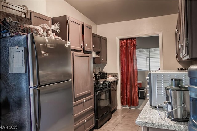 2001 E Mcwilliams Ave, Las Vegas, NV 89101 - kitchen with freestanding refrigerator, black gas range oven, light tile patterned floors, and under cabinet range hood