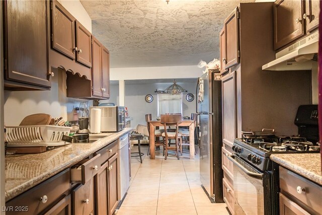 2001 E Mcwilliams Ave, Las Vegas, NV 89101 - kitchen featuring black range with gas cooktop, under cabinet range hood, freestanding refrigerator, light tile patterned flooring, and dishwasher