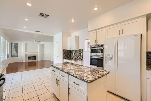 10241 Regents Cross Pl, Las Vegas, NV 89144 - kitchen featuring white refrigerator with ice dispenser, stainless steel double oven, tasteful backsplash, ceiling fan, and a kitchen island