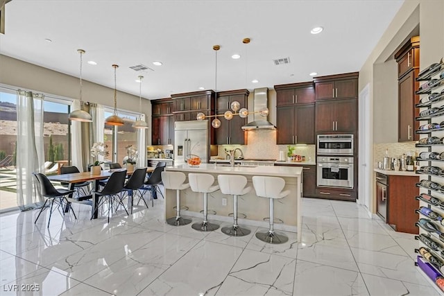 881 Barrhead Ave, Henderson, NV 89012 - kitchen with stainless steel appliances, wall chimney range hood, light countertops, backsplash, and a kitchen breakfast bar