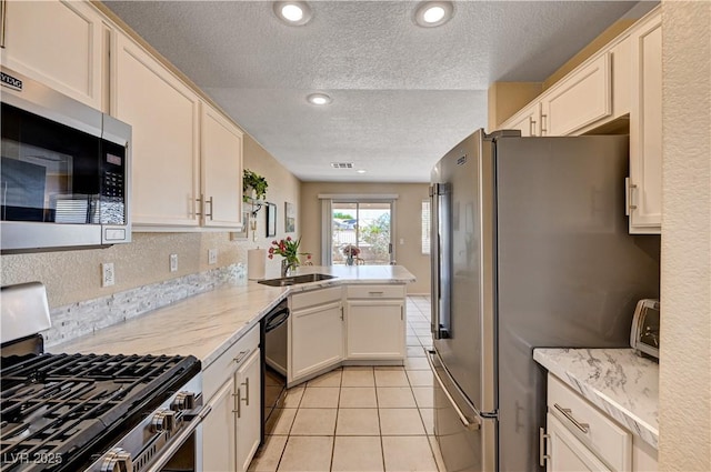 1902 Panther Pl, North Las Vegas, NV 89031 - kitchen with appliances with stainless steel finishes, a textured ceiling, light tile patterned floors, a peninsula, and light stone counters