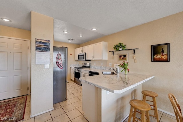 1902 Panther Pl, North Las Vegas, NV 89031 - kitchen with appliances with stainless steel finishes, a peninsula, a kitchen bar, white cabinetry, and light tile patterned flooring