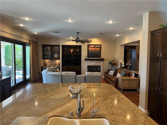 4208 Agosta Luna Pl, Las Vegas, NV 89135 - kitchen featuring light stone countertops, a stone fireplace, a ceiling fan, dark brown cabinetry, and a sink