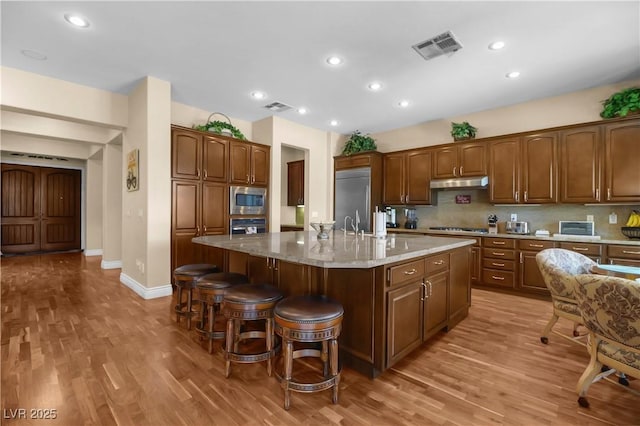 4208 Agosta Luna Pl, Las Vegas, NV 89135 - kitchen with built in appliances, light wood finished floors, under cabinet range hood, a breakfast bar, and recessed lighting