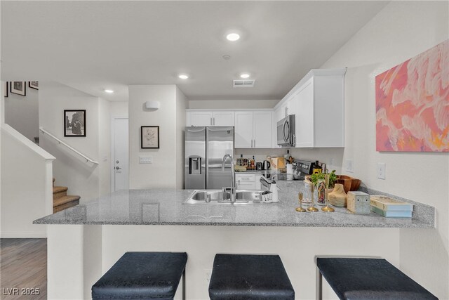 2598 Polar White Ave, North Las Vegas, NV 89086 - kitchen with appliances with stainless steel finishes, a sink, a peninsula, light stone countertops, and white cabinets