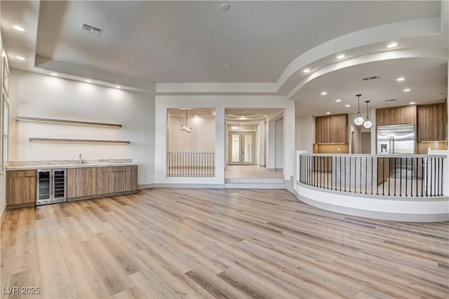 9921 Mirada Dr, Las Vegas, NV 89144 - unfurnished living room featuring wine cooler, light wood finished floors, bar area, recessed lighting, and a raised ceiling