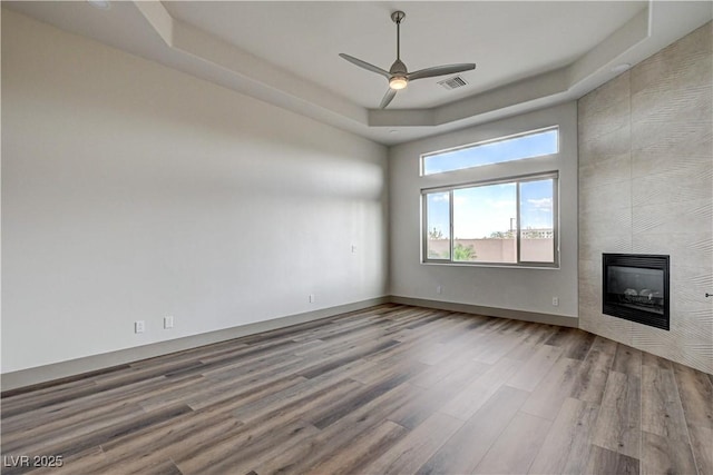 9921 Mirada Dr, Las Vegas, NV 89144 - unfurnished living room with wood finished floors, ceiling fan, a tiled fireplace, a raised ceiling, and baseboards