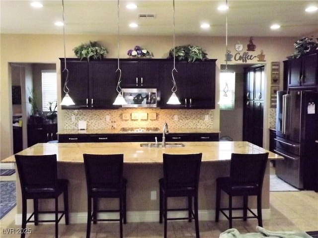 4242 Helena Hideaway Ct, Las Vegas, NV 89129 - kitchen with appliances with stainless steel finishes, a sink, decorative backsplash, a kitchen island with sink, and light stone counters