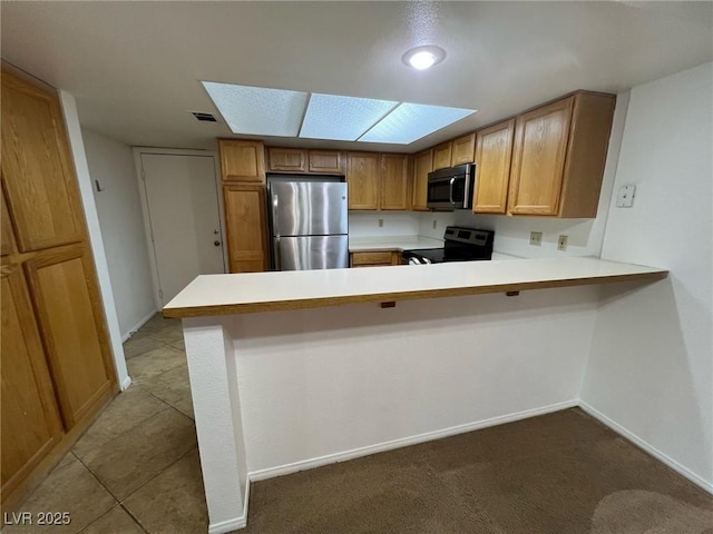 8940 Antioch Way, Las Vegas, NV 89117 - kitchen featuring stainless steel appliances, light countertops, a peninsula, a skylight, and brown cabinetry