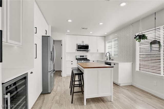 10554 Lilac Tree Ave, Las Vegas, NV 89135 - kitchen featuring appliances with stainless steel finishes, beverage cooler, a kitchen island, decorative backsplash, and light wood finished floors