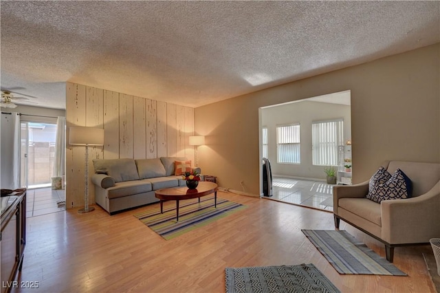 4445 Peterson Dr, Las Vegas, NV 89103 - living room with a textured ceiling, healthy amount of natural light, light wood-type flooring, ceiling fan, and wood walls