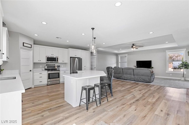 1395 Logandale Dr, Logandale, NV 89021 - kitchen featuring stainless steel appliances, light wood-style floors, recessed lighting, a tray ceiling, and a kitchen breakfast bar