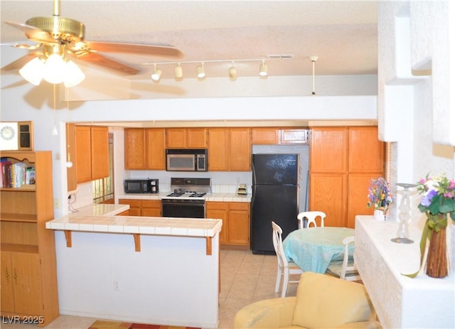 3519 W Red Coach Ave, North Las Vegas, NV 89031 - kitchen with black appliances, tile counters, a peninsula, ceiling fan, and light tile patterned floors