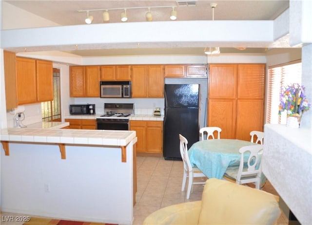 3519 W Red Coach Ave, North Las Vegas, NV 89031 - kitchen featuring black appliances, tile counters, a peninsula, light tile patterned floors, and track lighting