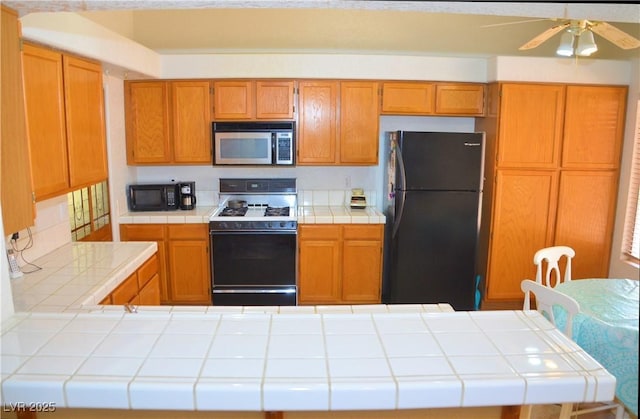 3519 W Red Coach Ave, North Las Vegas, NV 89031 - kitchen with black appliances, tile countertops, a ceiling fan, and brown cabinets