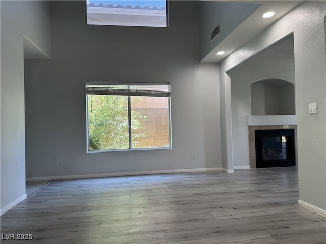 11029 Meadow Leaf Ave, Las Vegas, NV 89144 - unfurnished living room with wood finished floors, a glass covered fireplace, a towering ceiling, and baseboards