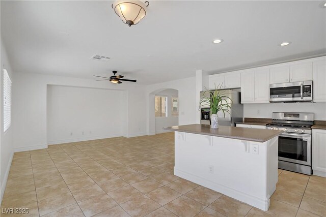 236 Dog Leg Dr, Las Vegas, NV 89148 - kitchen featuring stainless steel appliances, arched walkways, a kitchen island, light tile patterned floors, and white cabinetry