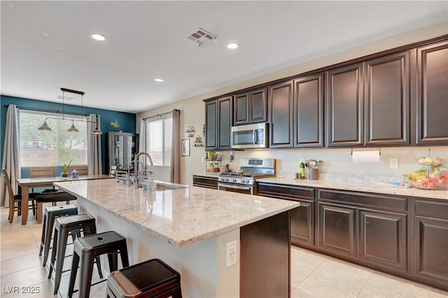 6334 Orions Belt Peak St, North Las Vegas, NV 89031 - kitchen with appliances with stainless steel finishes, a sink, light tile patterned floors, light stone countertops, and a breakfast bar