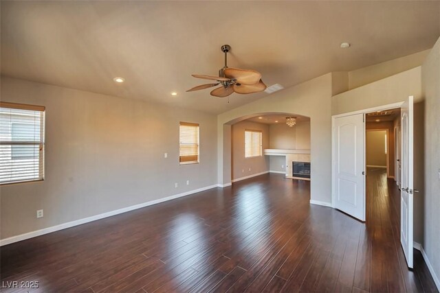 1740 Flores Ln, Henderson, NV 89012 - unfurnished living room with ceiling fan, a tile fireplace, baseboards, arched walkways, and dark wood-style flooring