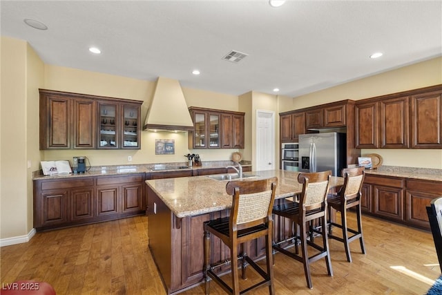 5747 Jaborandi Ave, Pahrump, NV 89061 - kitchen featuring premium range hood, black electric cooktop, stainless steel fridge, an island with sink, and light wood-style flooring