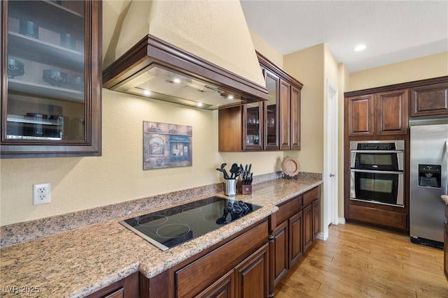 5747 Jaborandi Ave, Pahrump, NV 89061 - kitchen with appliances with stainless steel finishes, custom range hood, light wood-type flooring, light stone counters, and glass insert cabinets