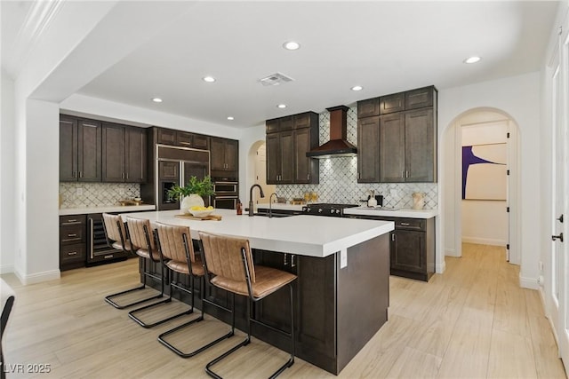 11775 Woodbrook Ct, Las Vegas, NV 89141 - kitchen featuring wall chimney range hood, arched walkways, decorative backsplash, a kitchen bar, and light countertops