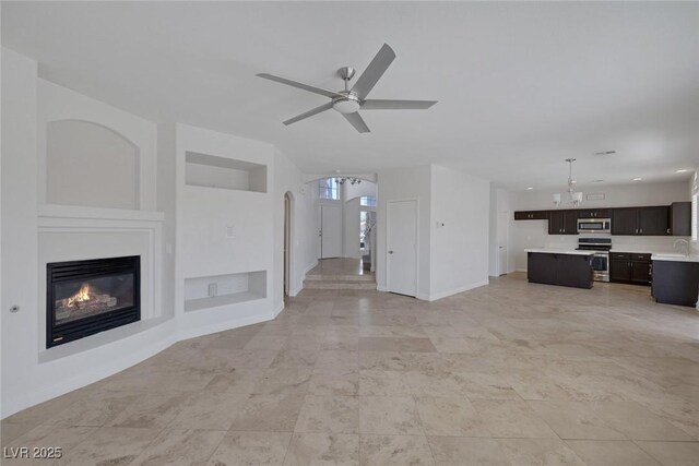 829 Dancing Vines Ave, Las Vegas, NV 89183 - unfurnished living room featuring built in features, ceiling fan, baseboards, a sink, and a glass covered fireplace