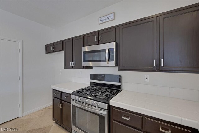 829 Dancing Vines Ave, Las Vegas, NV 89183 - kitchen featuring appliances with stainless steel finishes, tile counters, dark brown cabinetry, and baseboards