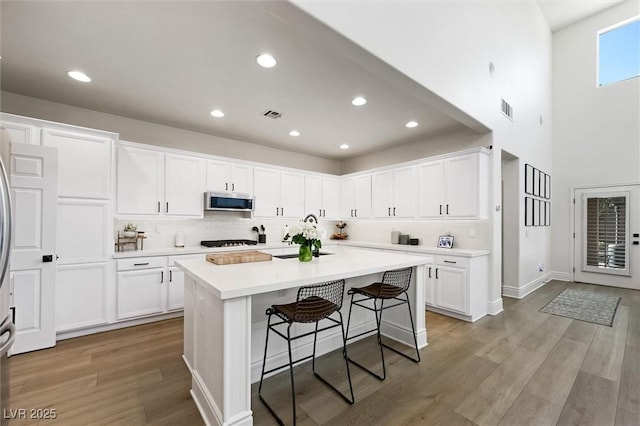 11340 Espadrille Ct, Las Vegas, NV 89138 - kitchen featuring stainless steel microwave, white cabinets, backsplash, a breakfast bar area, and recessed lighting