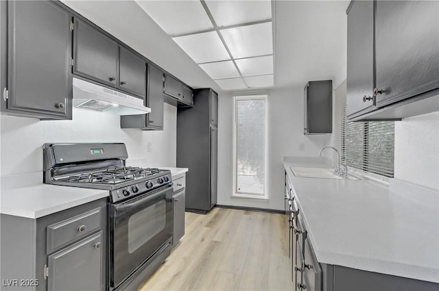 1390 Vegas Valley Dr Unit 26, Las Vegas, NV 89169 - kitchen with black gas range, under cabinet range hood, a sink, light wood finished floors, and light countertops