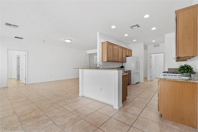 7448 Lintwhite St, North Las Vegas, NV 89084 - kitchen with freestanding refrigerator, light tile patterned flooring, light stone counters, recessed lighting, and brown cabinets