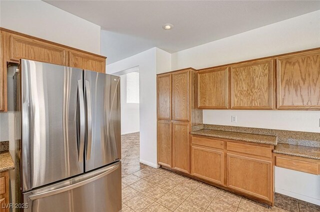 74 Harbor Coast St, Las Vegas, NV 89148 - kitchen featuring freestanding refrigerator, brown cabinetry, light tile patterned flooring, and light stone countertops