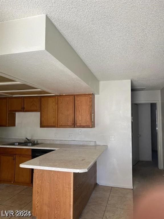 4720 Obannon Dr Unit D, Las Vegas, NV 89102 - kitchen with a sink, a peninsula, a textured ceiling, brown cabinetry, and light tile patterned flooring
