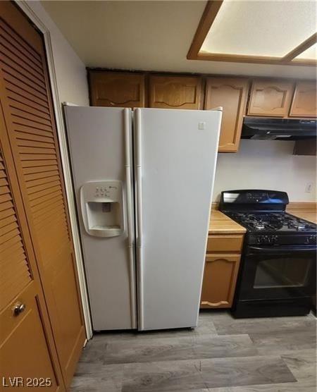 854 Stainglass Ln, Las Vegas, NV 89110 - kitchen with white refrigerator with ice dispenser, black range with gas cooktop, under cabinet range hood, and light countertops