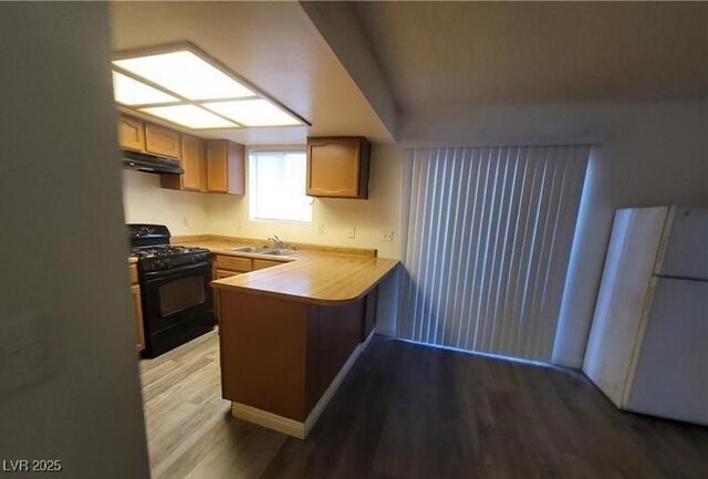 854 Stainglass Ln, Las Vegas, NV 89110 - kitchen with black range with gas stovetop, under cabinet range hood, freestanding refrigerator, a sink, and a peninsula