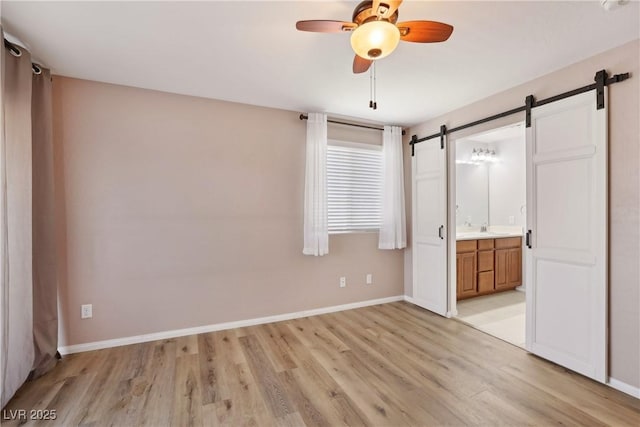 9053 Entrancing Ave, Las Vegas, NV 89149 - unfurnished bedroom featuring a barn door, light wood-style floors, baseboards, and ensuite bathroom