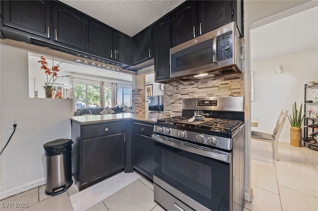 1916 Canosa Ave, Las Vegas, NV 89104 - kitchen featuring appliances with stainless steel finishes, a textured ceiling, dark cabinets, decorative backsplash, and light tile patterned floors