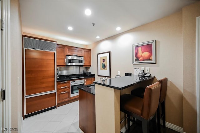 135 E Harmon Ave Unit 2420, Las Vegas, NV 89109 - kitchen featuring stainless steel appliances, dark countertops, a peninsula, brown cabinets, and a kitchen bar