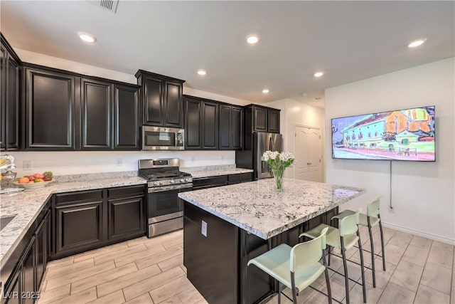 12286 Silvana St, Las Vegas, NV 89141 - kitchen featuring appliances with stainless steel finishes, a kitchen island, a kitchen bar, light stone counters, and dark cabinetry